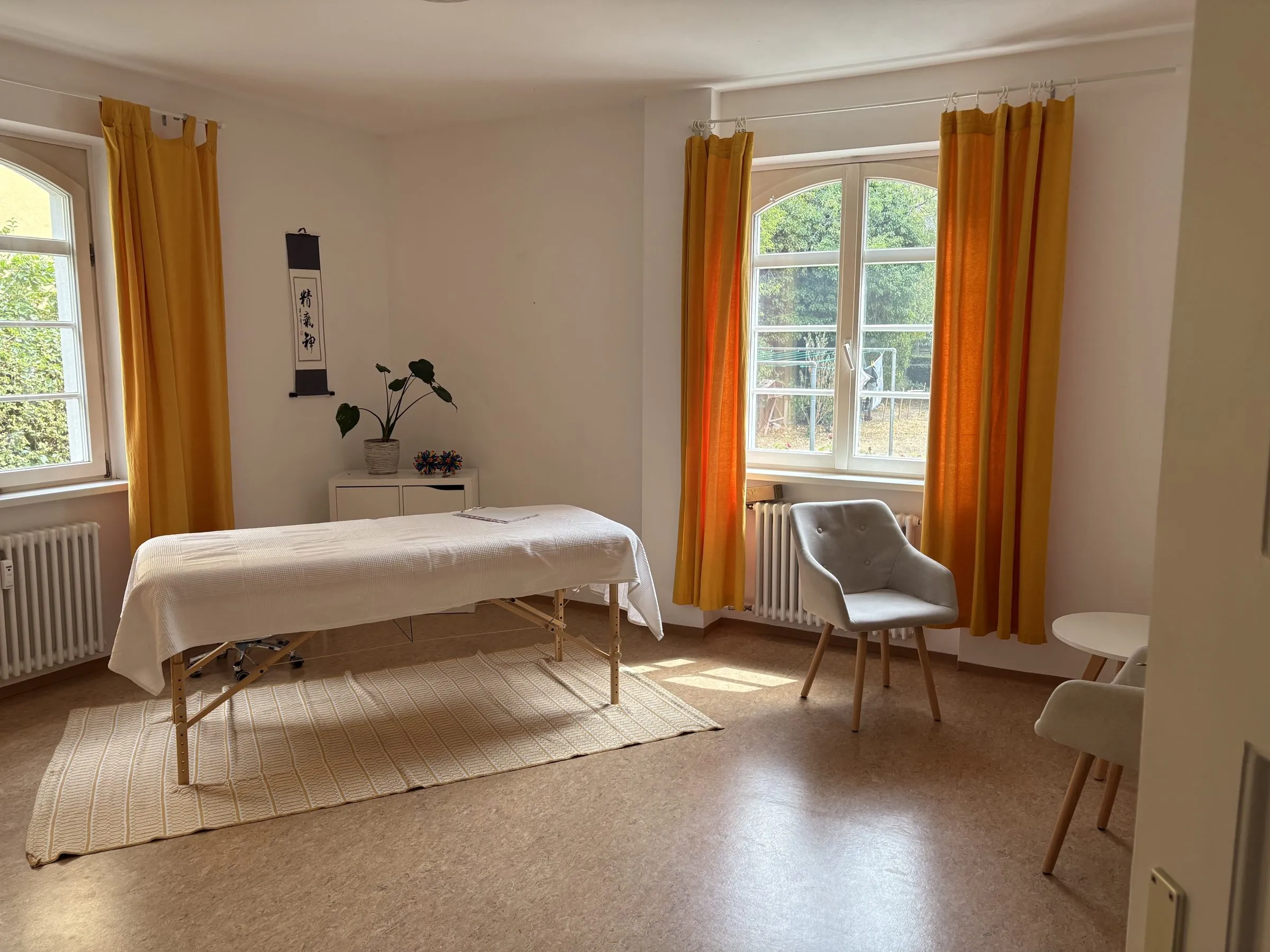 Der Praxisraum mit Behandlungsliege und zwei Rundbogenfenstern in der Fichtestr. 29 in Freiburg